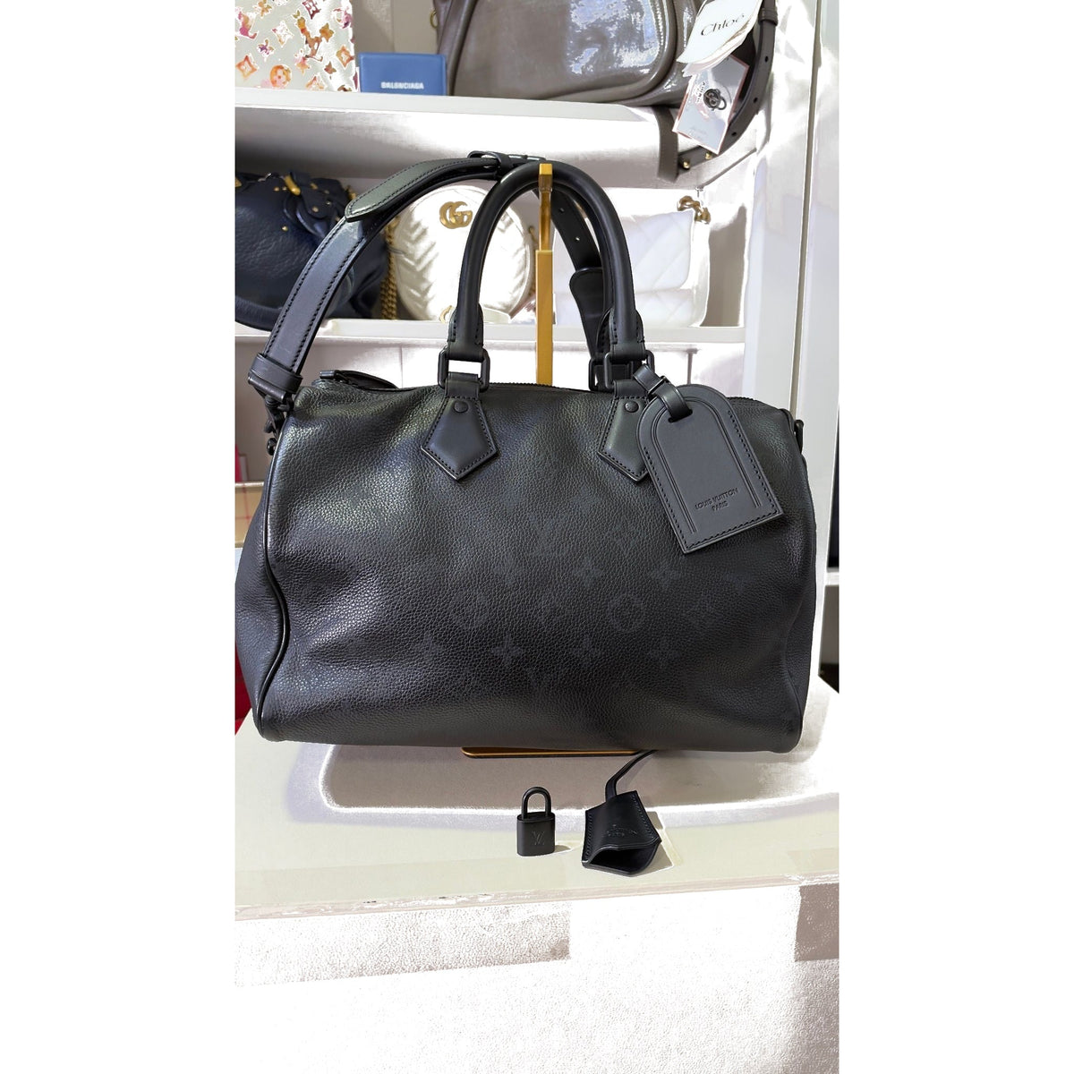 Front view of the Speedy 30 P9 Bandouliere with leather luggage tag; padlock and clochette on the shelf below